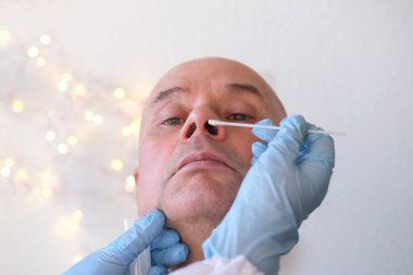 Yaşlı, kel bir adamın yüzü, laboratuvar asistanı, doktor burun mukozasından koronavirüs, DNA tespiti, COVID-19 konsepti için örnek alıyor.