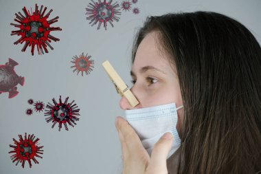 Genç bir kadın, uzun sarı saçlı, beyaz bir maske takmış, burnu tahta bir mandalla kenetlenmiş, konsept berbat, koronavirüs yüzünden koku kaybı, grip.