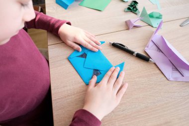 Japon origami tekniği, el sanatları, hobiler, oyunlar, odadaki aktiviteler, iyi motor becerilerin geliştirilmesi gibi konuları kullanarak beyaz kağıttan katlanmış çocuk, çocuk ve çocuk.