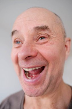 Avrupalı yaşlı bir adamın yüzü, yaşlanan cildinde kırışıklıklar, neşeyle gülme, ağzını açma, iyi ruh hali, kozmetoloji, yaşla ilgili değişiklikler.