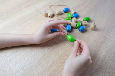 Küçük çocuk, ipe renkli tahta boncuklar dizen çocuk, çocuk parmakları yakın plan, iyi motor becerilerin gelişimi konsepti, dokunsal hisler, yaratıcılık, çocuk eğlencesi