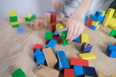 Küçük çocuk, çocuk renkli ahşap küplerle oynuyor, evler ve roketler yapıyor, yaratıcılığın gelişimi, motor beceriler, sabır ve azim kavramı.