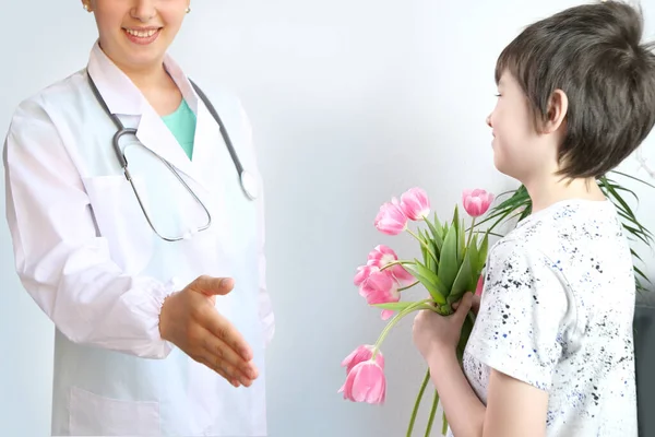 child, boy of 8-10 years old holds a bouquet of pink tulips in his hands, a doctor in white coat with stethoscope, concept of giving fresh flowers, doctor\'s day, birthday, little patient\'s gratitude