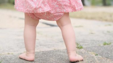 Küçük bir kız, elbise ve panama giymiş bir bebek çimlerin üzerinde yürüyor, ilk adımların konsepti, mutlu çocukluk, çocuk oyunları, alfa jenerasyonu