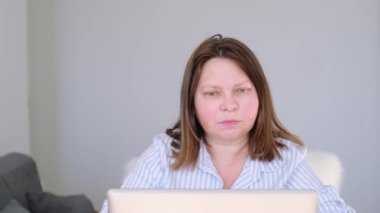 Açık renk bluzlu yaşlı bir kadın evde dizüstü bilgisayar başında oturuyor, internette geziniyor, okuyor, çok şaşırıyor, duygusal tepki veriyor, konsept şok içeriği, korkunç haberler.