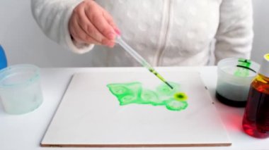 Kadın yeşil boyayı bir pipetle uyguluyor, şişiriyor, beyaz bir yüzeye yayılmış soyut lekeler, suluboya, alkol mürekkebi, tasarımcı için arka plan, sanat terapisi.