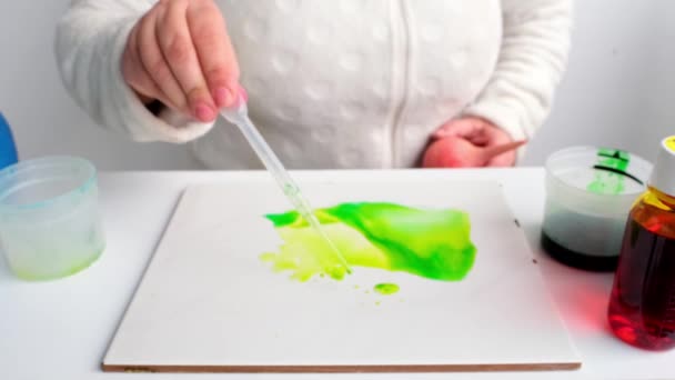 女性は緑のペンキをピペットで塗り膨張させ白い表面に抽象的な斑点を広げ水彩やアルコールインクで絵を描き — ストック動画