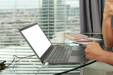 Adam bir dizüstü bilgisayarın arkasında çalışıyor. Modern Avrupa şehrinin penceresinin önündeki bir ofiste boş ekranla. İş fikirleri konsepti, işyeri.