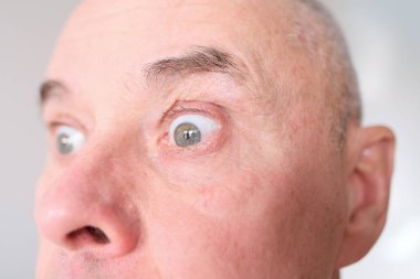 60 'lı yaşlarda beyaz bir adamın gri gözünün önünde güçlü kırışıklıklar, yüzünde parlak duygular, erkek cilt bakımı kavramı.