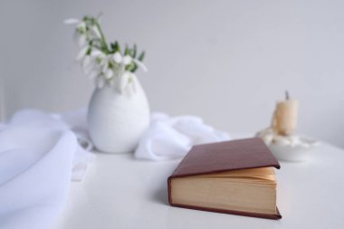 Yüksek anahtar tarzında bir hayat, beyaz masada koyu kırmızı bir ciltte eski bir kağıt kitap, mum, vazoda yarım kardelen buketi, mevsimleri değiştirme konsepti, edebiyat okuma.