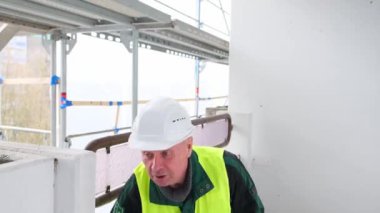 Neşeli kıdemli erkek ustabaşı, beyaz şapkalı işçi, iş kıyafetleri içinde komik dans ediyor ve inşaat sahasında eğleniyor çılgın işçiler, binaların onarımı, yapılar