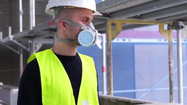 İnşaat alanındaki teftiş sırasında beyaz şapkalı ve koruyucu solunum cihazlı genç erkek ustabaşı, işçi veya mimar, binaların ve yapıların onarımını izleme konsepti,