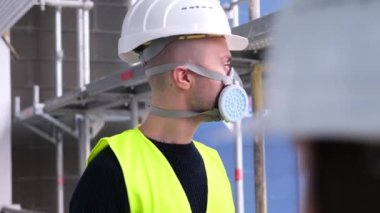 İnşaat alanındaki teftiş sırasında beyaz şapkalı ve koruyucu solunum cihazlı genç erkek ustabaşı, işçi veya mimar, binaların ve yapıların onarımını izleme konsepti,