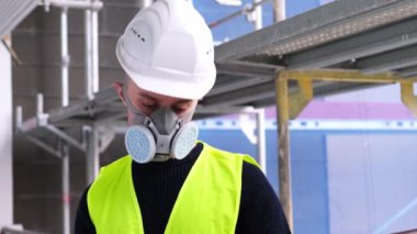 İnşaat alanındaki teftiş sırasında beyaz şapkalı ve koruyucu solunum cihazlı genç erkek ustabaşı, kadın geliyor, belgeleri imzalıyor, binaların onarımını izleme konseptini inceliyor.