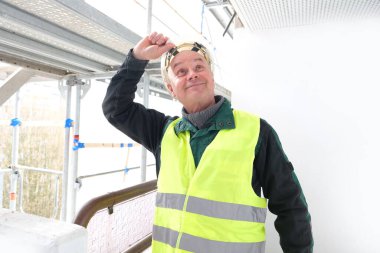 Neşeli kıdemli erkek ustabaşı, beyaz kazaklı işçi, inşaat alanında iş kıyafetleri, çılgın işçiler, bina onarımı konsepti, yapılar.