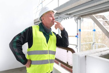 Erkek ustabaşı, beyaz şapkalı işçi, inşaat sahasında duruyor. Binaların, binaların, yapıların, iskelelerin tamiri kavramı...