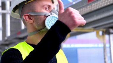 İnşaat alanındaki teftiş sırasında beyaz başlıklı ve koruyucu solunum cihazlı genç erkek ustabaşı, mühendis veya mimar, binaların ve yapıların onarımını izleme konsepti,