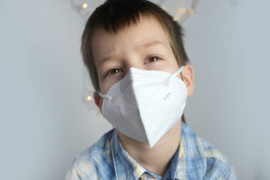 Küçük bir çocuk, 7-8 yaşlarında, beyaz maske sınıfında FFP2, yakın çekim yüzü, tıbbi konsept, karantina, COVID-19, coronavirus konsepti