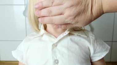 Küçük çocuk, bebek, sarışın kız gülümsüyor, kafasının bir kısmı yakın plan, kadın eli ağzını kapatıyor, konuşma yasağı konsepti, çocukluk şakaları, alaycılar.