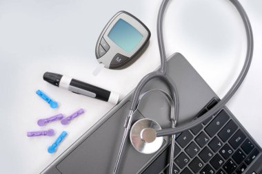 Tıbbi stetoskop, yedek iğneler, glukometre, beyaz arka planda dizüstü bilgisayar klavyesi, evdeki kan şekerini ölçmek için ekipman