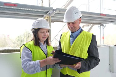 Deneyimli yaşlı mimar, beyaz kaskı koruyan kadın mühendis nesneyi kabul et, inşaat alanında belge imzala, inşaat mühendisliği kavramı, işbirliği