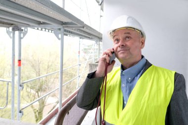 Tecrübeli bir inşaatçı, inşaat ekibi şefi, miğfer koruma mühendisi inşaat inşaatı için inşaat alanında telefonla konuşuyor, inşaat mühendisliği konsepti.