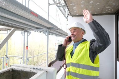 Tecrübeli bir inşaatçı, inşaat ekibi şefi, miğfer koruma mühendisi inşaat inşaatı için inşaat alanında telefonla konuşuyor, inşaat mühendisliği konsepti.