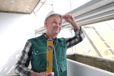 Koruyucu beyaz kasklı ve işçi üniformalı yaşlı inşaatçı inşaat ve onarım için inşaat alanında duruyor. İnşaat mühendisliği konsepti.