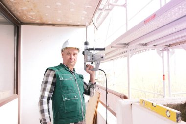 Koruyucu beyaz kasklı ve işçi üniformalı yaşlı inşaatçı inşaat ve onarım için inşaat alanında duruyor. İnşaat mühendisliği konsepti.