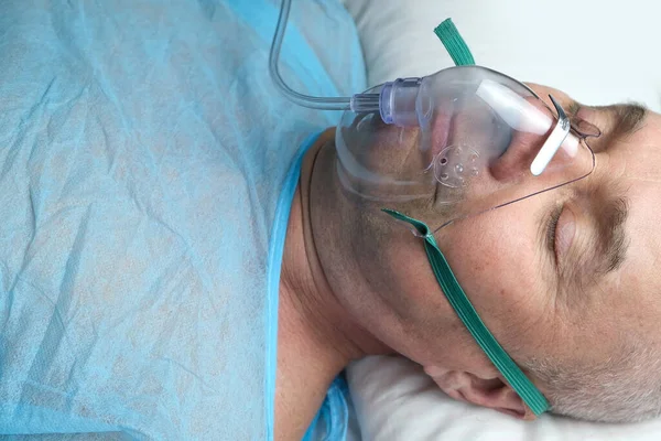 elderly man patient in a blue shirt lies in a facial oxygen mask, the concept of medical care, anesthesiology and intensive care, oxygen therapy, resuscitation procedures