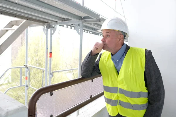 experienced elderly builder, construction team chief, construction engineer in helmet protection talking on phone at construction site for building renovation, civil engineering concept