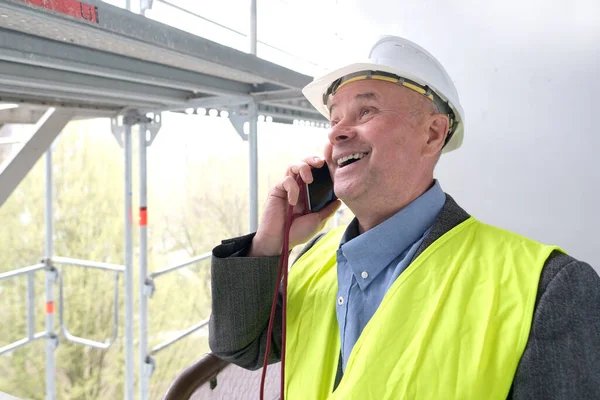 experienced elderly builder, construction team chief, construction engineer in helmet protection talking on phone at construction site for building renovation, civil engineering concept