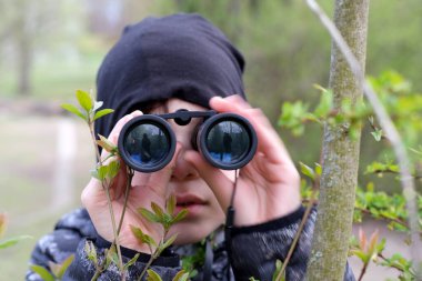 Çocuk, 8-10 yaşlarındaki sapık parkta siyah dürbünlere bakıyor, casuslar, sırları avlıyor, ormanda kayboluyor, tehlikeli macera, gözetleme konsepti, insan ve hayvanları gözlemleme.