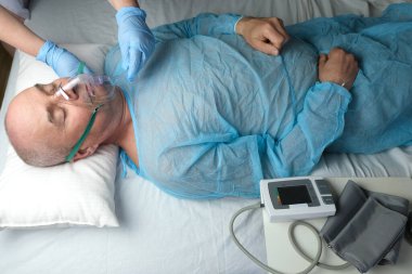 Mavi gömlekli yaşlı adam yalan söylüyor, doktor maske takıyor, tıbbi bakım konsepti, anestezi ve yoğun bakım, oksijen terapisi, koronavirüs tedavisi, COVID-19