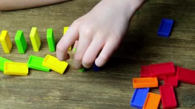 Çocuk elinin yakın çekimi domino taşlarının çizgilerini oluşturur, renkli domino taşları birbiri ardına düşer, iş dünyasında domino etkisi kavramı, eğitim, iyi motor becerilerin gelişimi