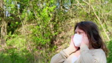 50 yaşında, bej bluzlu yetişkin Avrupalı bir kadın yeşil parkta maske takarak, yüksek dereceli koruma sınıfı FFP2, Avrupa 'da COVID-19 Coronavirus, grip, enfeksiyon içeren koruyucu solunum cihazıyla yürüyor.