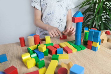 Küçük çocuk, çocuk renkli ahşap küplerle oynuyor, evler ve roketler yapıyor, yaratıcılığın gelişimi, motor beceriler, sabır ve azim kavramı.