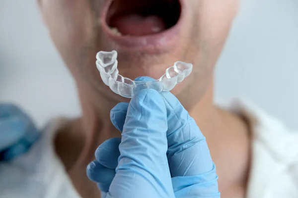 closeup male doctor conducts an examination of oral cavity of old male patient, tries on Silicone Night Mouth Guard for Teeth Clenching Grinding Dental Bite Sleep Aid, concept of dental services