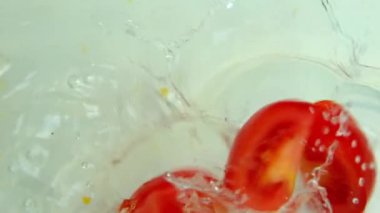 Süper yavaş çekimde kırmızı domates dilimleri suya düşer, ters döner, uçan su sıçratır, vejetaryen diyeti kavramı, sağlıklı yiyecekler, sıcakta ferahlatıcı.