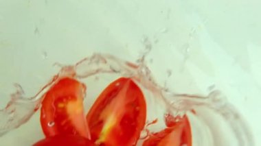 Süper yavaş çekimde kırmızı domates dilimleri suya düşer, ters döner, uçan su sıçratır, vejetaryen diyeti kavramı, sağlıklı yiyecekler, sıcakta ferahlatıcı.