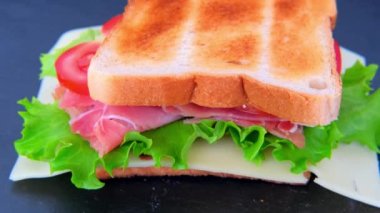 Aperatif bir sandviçin yanında olgun domates dilimleri, yeşil salata, peynir, jambon, kızarmış tost, hızlı atıştırma konsepti, evde fast food pişirme, şef sandviçi hazırlama, seçici odaklanma.