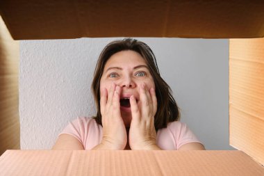 Kadın, sipariş edilmiş ürünle birlikte bir karton kutu açtı ve içindekilere duygusal tepki verdi. Posta eşyası, paket, internetten mal satın alma, sürpriz.