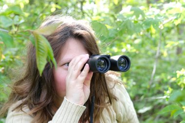 Yakın plan meraklı Avrupalı yetişkin kadın elinde zoom ile siyah gözlük tutuyor, yeşillikte saklanıyor, yeşil çalılıklardan gözetliyor, sadakatsiz kocasını gözetliyor, komşularını gözetliyor.