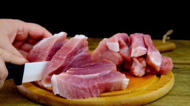 Kadın eli, dilimlere ayrılmış porselen et bıçağı kullanıyor. Yuvarlak kesim tahtasında domuz eti doğranmış biftek, ev yemeği konsepti, protein besin maddesi, ahşap arka plan.