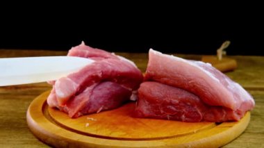 Kadın eli, dilimlere ayrılmış porselen et bıçağı kullanıyor. Yuvarlak kesim tahtasında domuz eti doğranmış biftek, ev yemeği konsepti, protein besin maddesi, ahşap arka plan.
