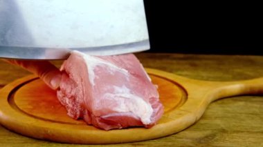 Kadın elleri et dilimleri için metal bir balta kullanıyor. Yuvarlak kesim tahtasında domuz eti, ev yemeği konsepti, protein besin maddesi, ahşap arka plan.