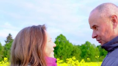 Erkek ve kadın, yaşlı bir çift kolza tarlaları arasında iletişim kuruyor, neşe, sarılma, aile ilişkileri, sevgi, şefkat kavramı.