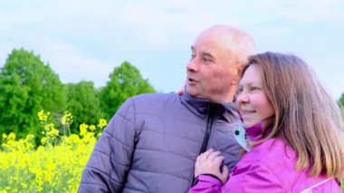 Erkek ve kadın, yaşlı bir çift kolza tarlaları arasında iletişim kuruyor, neşe, sarılma, aile ilişkileri, sevgi, şefkat kavramı.