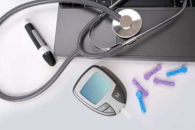 Tıbbi stetoskop, yedek iğneler, glukometre, beyaz arka planda dizüstü bilgisayar klavyesi, evdeki kan şekerini ölçmek için ekipman