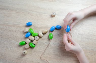 Küçük çocuk, ipe renkli tahta boncuklar dizen çocuk, çocuk parmakları yakın plan, iyi motor becerilerin gelişimi konsepti, dokunsal hisler, yaratıcılık, çocuk eğlencesi